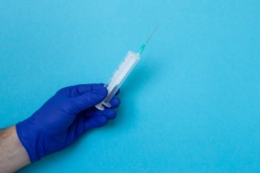 Doktorun elleri mavi arka plan, koronavirüs, hastalık, enfeksiyon ve karantina üzerinde şırınga tutuyor.