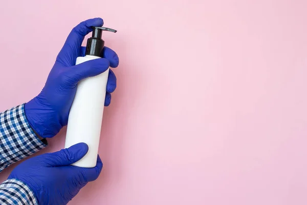 antibacterial hand sanitizer on hands isolated on pink, blue gloves on hands