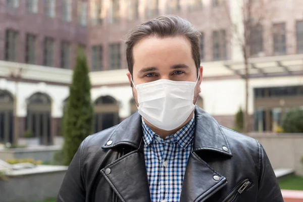 portrait of man in a medical mask on a background of a modern building, coronavirus, illness, infection, quarantine, medical mask
