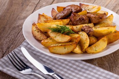 Baharatlı kızarmış patates ve et otlar ve baharatlar ile beyaz tabak içinde görev yaptı. Üstten Görünüm ahşap masa üzerinde. Çatal, bıçak ve havlu.
