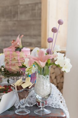 Bir şekilde dekore edilmiş tatlı masada bir kek, şeker, şekerleme, cakepops, meyve, meyve suyu ve çiçek var.