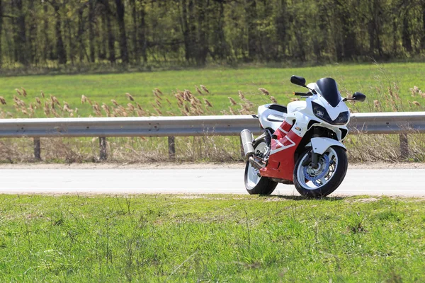 Un motocycliste se tient sur le bord d'une route vide par une journée ensoleillée. Beaucoup d'herbe verte sur le fond. Personne. — Photo