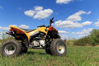 Bir dört tekerlekli sarı Atv quad-ağaçlar ve mavi gökyüzü bulutlu arka planda yeşil çimenlerin üzerinde boşta duran Bisiklet