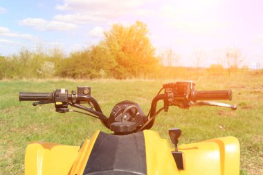 tekerlek direksiyon dört tekerlekli sarı Atv quad-ağaçlar ve mavi gökyüzü bulutlu arka planda yeşil çimenlerin üzerinde boşta duran Bisiklet görünümü