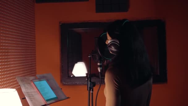 Mooie witte meisje hoofdtelefoon dragen en zingen in de microfoon in de opnamestudio — Stockvideo