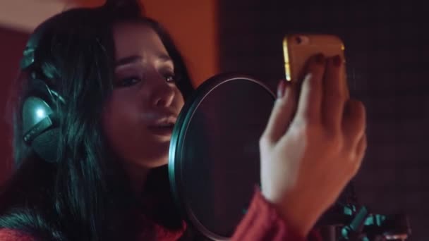 Молодая женщина в наушниках в студии звукозаписи возле микрофона . — стоковое видео