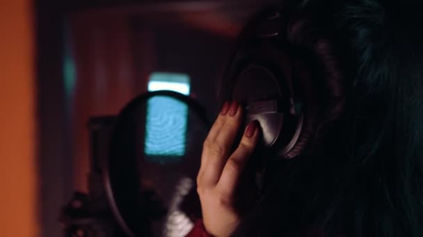 Junge Frau trägt Kopfhörer im Tonstudio in der Nähe des Mikrofons. — Stockvideo