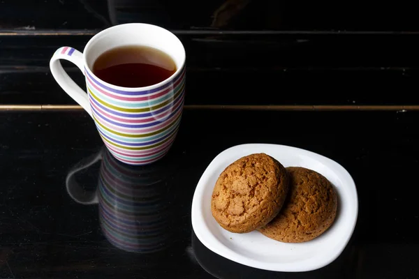 On a black background two oatmeal cookies lie on a white plate, — Stock Photo, Image