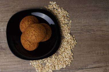 dağınık yulaf yanında siyah bir plaka üzerinde üç yulaf ezmeli kurabiye yalan