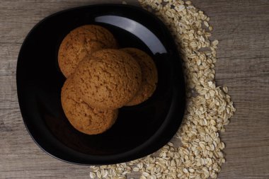 dağınık yulaf yanında siyah bir plaka üzerinde üç yulaf ezmeli kurabiye yalan