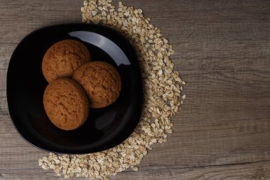 dağınık yulaf yanında siyah bir plaka üzerinde üç yulaf ezmeli kurabiye yalan