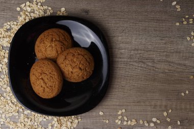 dağınık yulaf yanında siyah bir plaka üzerinde üç yulaf ezmeli kurabiye yalan