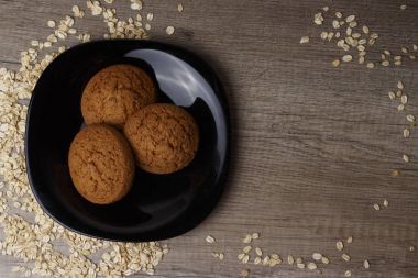 dağınık yulaf yanında siyah bir plaka üzerinde üç yulaf ezmeli kurabiye yalan