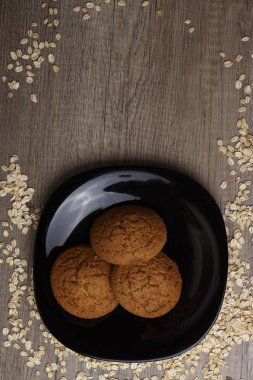 dağınık yulaf yanında siyah bir plaka üzerinde üç yulaf ezmeli kurabiye yalan