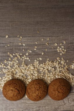 dağınık yulaf yanında siyah bir plaka üzerinde üç yulaf ezmeli kurabiye yalan