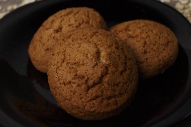 dağınık yulaf yanında siyah bir plaka üzerinde üç yulaf ezmeli kurabiye yalan