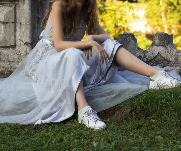 Flicka i en klänning och sneakers sitter på gräset — Stockfoto