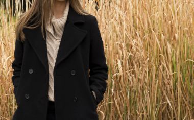 bir kız siyah paltolu kurutulmuş bir arka plan karşı duruyor 