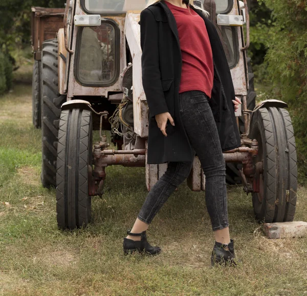 A girl in a black coat and a red jacket is standing near a tract — Stock Photo, Image