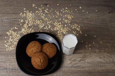 dağınık yulaf yanında siyah bir plaka üzerinde üç yulaf ezmeli kurabiye yalan