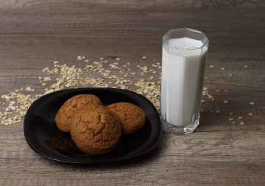 dağınık yulaf yanında siyah bir plaka üzerinde üç yulaf ezmeli kurabiye yalan