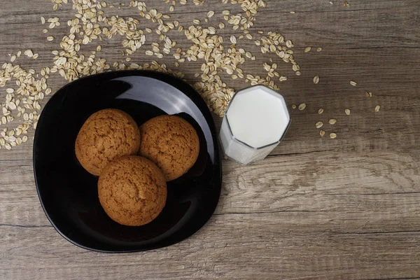 dağınık yulaf yanında siyah bir plaka üzerinde üç yulaf ezmeli kurabiye yalan