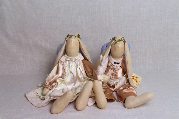 Two toy rabbits, an angel, in beige outfits sit on the background — Stock Photo, Image