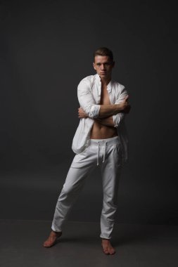 gri bir arka plan üzerinde çıplak bir gövde, beyaz pantolon ve beyaz gömlek, bir adamla standları