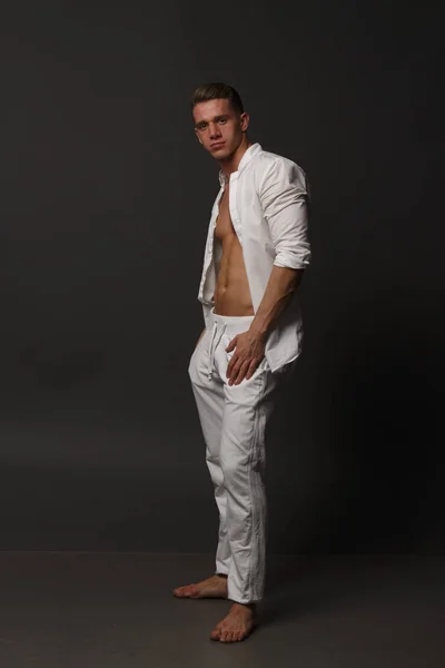 Ein Typ mit nacktem Oberkörper, weißer Hose und weißem Hemd steht auf grauem Hintergrund — Stockfoto