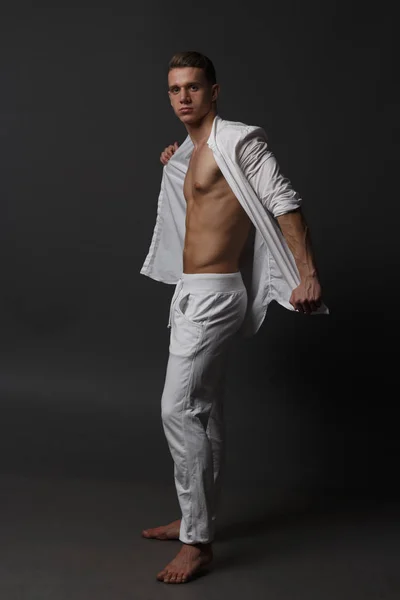 Ein Typ mit nacktem Oberkörper, weißer Hose und weißem Hemd steht auf grauem Hintergrund — Stockfoto