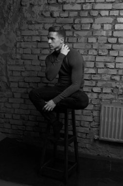 bir gri tuğla duvar, siyah-beyaz fotoğraf yakın bir sandalyede oturan beyaz genç adam