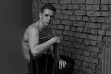 bir gri tuğla duvar, siyah-beyaz fotoğraf yakın bir sandalyede oturan beyaz genç adam