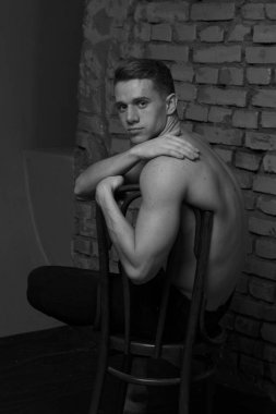 bir gri tuğla duvar, siyah-beyaz fotoğraf yakın bir sandalyede oturan beyaz genç adam