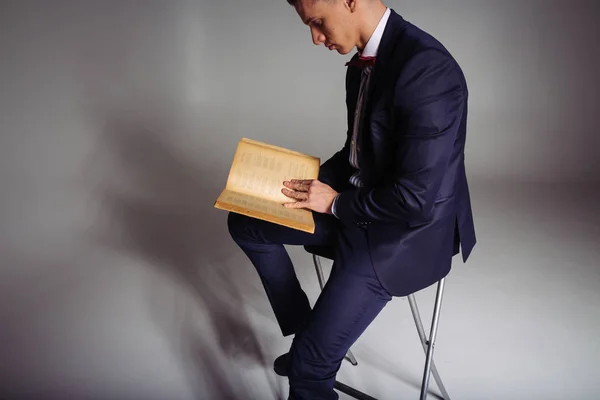 Un uomo, un ragazzo in abito blu, si siede su una sedia e legge un vecchio libro, il concetto di conoscenza, studio, scienza, affari, tutto nuovo, è un vecchio ben dimenticato — Foto Stock