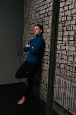 Beyaz bir çekici adam bir tuğla duvar arka plan Mavi kazak ve siyah pantolon giymiş