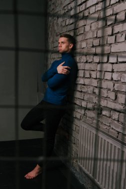 bir esir parmaklıklar arkasına taştan bir duvar yakınındaki Mavi kazak ve siyah pantolon, yalınayak beyaz çekici adam standları