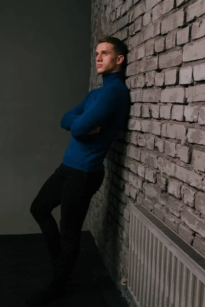 Beyaz bir çekici adam bir tuğla duvar arka plan Mavi kazak ve siyah pantolon giymiş — Stok fotoğraf