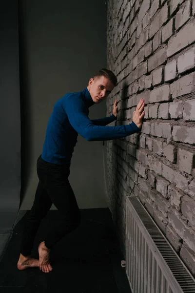 Bianco attraente ragazzo è vicino un muro di mattoni sfondo vestito con un maglione blu e pantaloni neri — Foto Stock