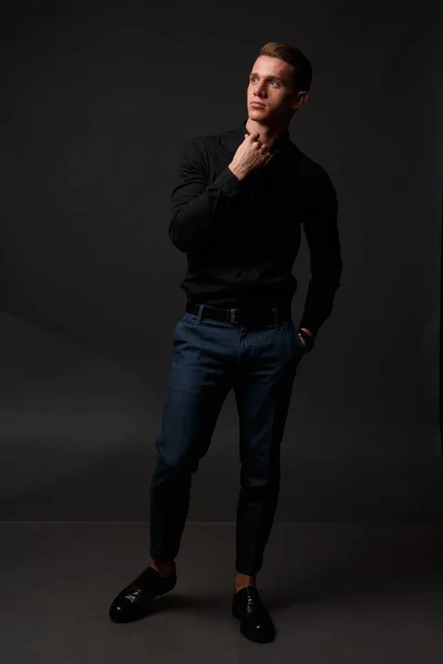 Karanlık bir arka plan üzerinde siyah gömlek ve Mavi pantolon çekici beyaz adam standları — Stok fotoğraf