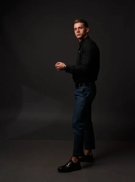 Karanlık bir arka plan üzerinde siyah gömlek ve Mavi pantolon çekici beyaz adam standları — Stok fotoğraf