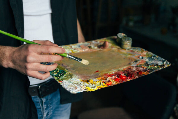 artist brush mix color oil painting on palette is holding in his hand closeup