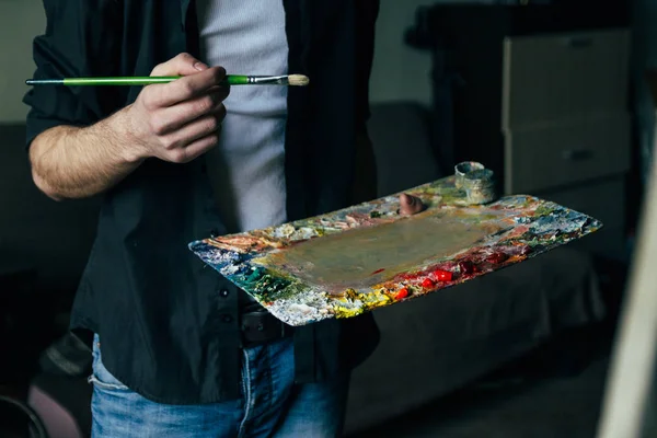 Artista pincel mezcla de color pintura al óleo en la paleta está sosteniendo en su mano primer plano —  Fotos de Stock
