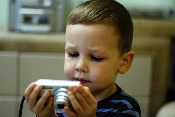 Een kleine jongen houdt van een camera in zijn handen en kijkt op het scherm — Stockfoto