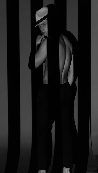 Mann mit Hut und nacktem Oberkörper steht zwischen schwarzen und weißen Streifen, Schwarz-Weiß-Foto — Stockfoto