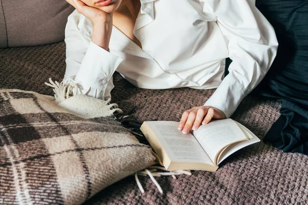 Menina lendo um livro em um cobertor quente. mulher mente, deite-se na cama, um cobertor, um sofá, um sofá e segura um livro. Menina lendo um livro — Fotografia de Stock