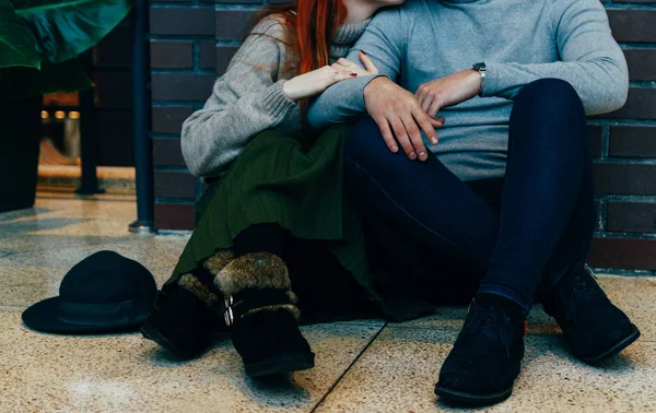 Sitzt das Paar in einer Umarmung auf dem Boden. Umarmung. eine weibliche Hand mit einem Ring, eine männliche Hand mit einer Uhr. Reden. graue Pullover. — Stockfoto