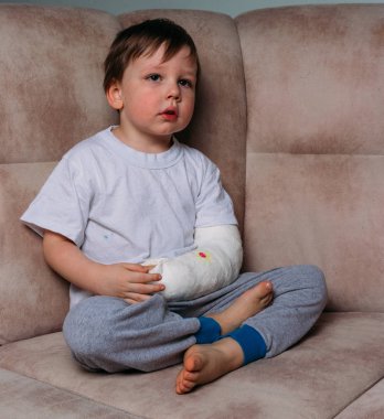 küçük bir çocuk alçıda kırık bir kol ile bir sandalyede oturuyor. hastane. Tıp. tehlike. ağrı. bacaklarda kırmak için. şiddet.