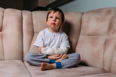 küçük bir çocuk alçıda kırık bir kol ile bir sandalyede oturuyor. hastane. Tıp. tehlike. ağrı. bacaklarda kırmak için. şiddet.