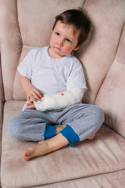 一个小男孩坐在椅子上, 胳膊断了, 在石膏上。医院。医学。危险。痛苦。折断四肢。暴力. — 图库照片