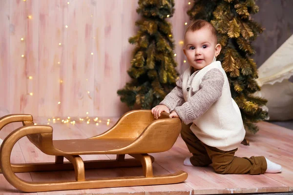 Um menino perto das árvores de Natal em um trenó, luzes de Natal, alegrias e sorrisos, peças de teatro. férias e férias — Fotografia de Stock